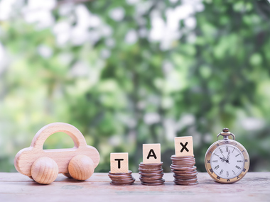 Stacks of coins spelling tax beside a wooden toy car and clock, symbolizing tax planning services from a Grand Junction CPA firm