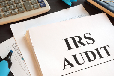 IRS audit paperwork on a desk with a calculator, highlighting payroll tax mistakes that can trigger audits for businesses.